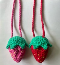 two crocheted strawberry purses on a white surface