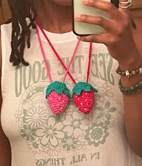 a woman taking a selfie with two crocheted strawberry necklaces